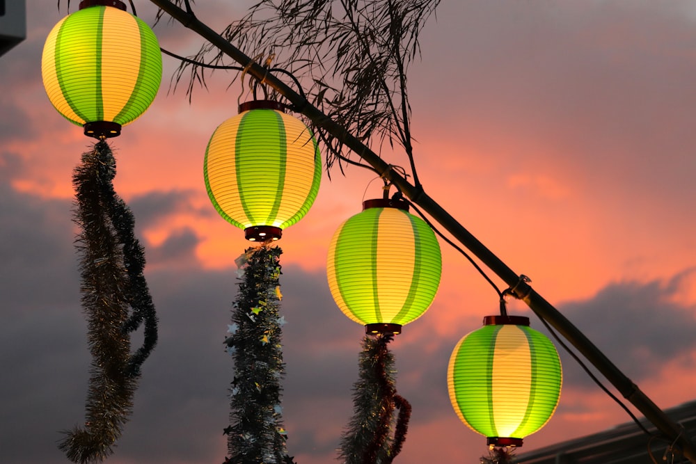 three yellow lanterns hanging from a tree with a pink sky in the background