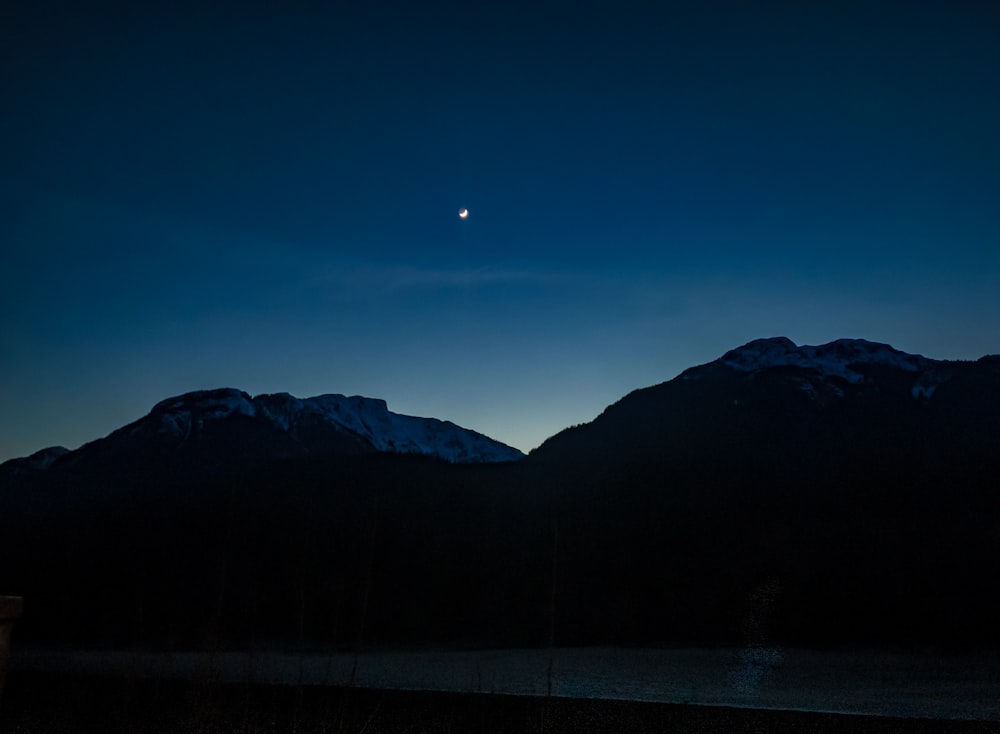 a view of a mountain range at night with the moon in the sky