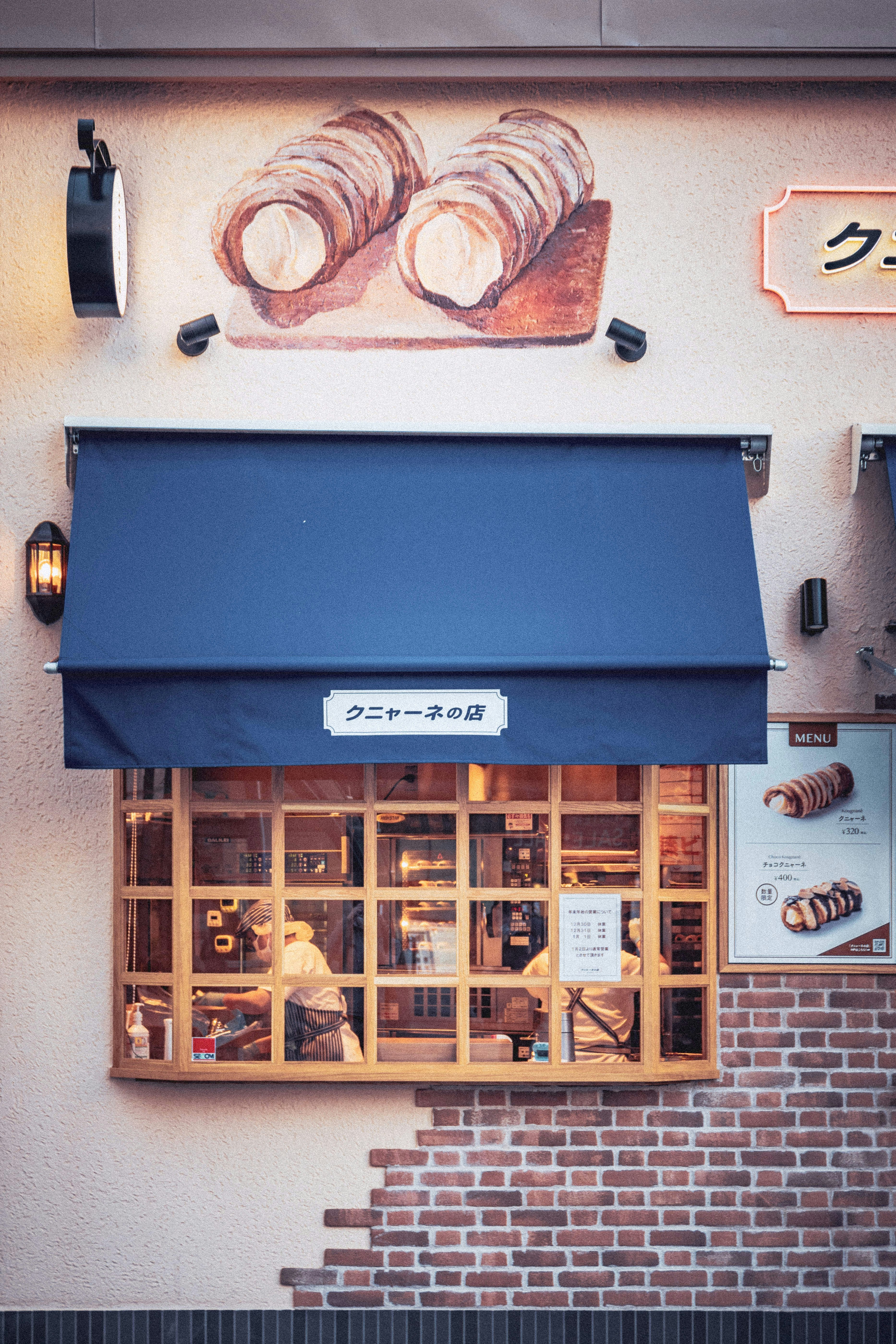 a store front with a blue awning and a painting of bread on the wall