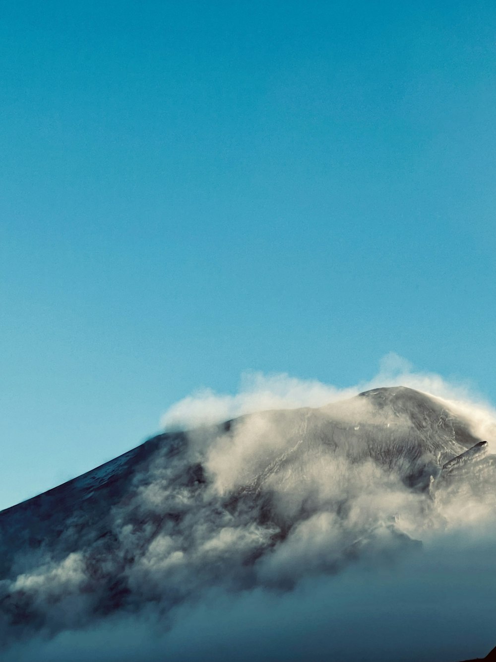 a mountain covered in clouds under a blue sky