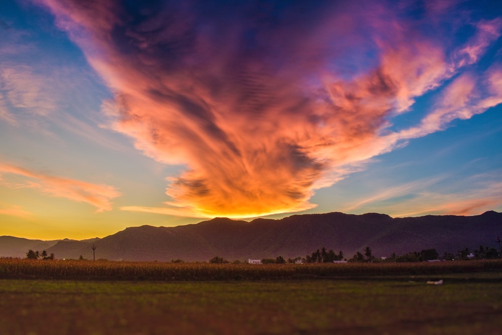 a beautiful sunset over a field with mountains in the background