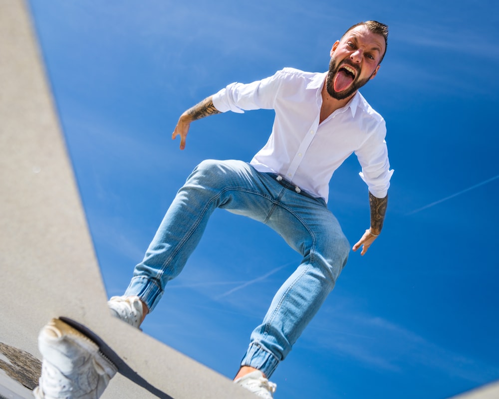 a man in white shirt and jeans doing a trick on a skateboard