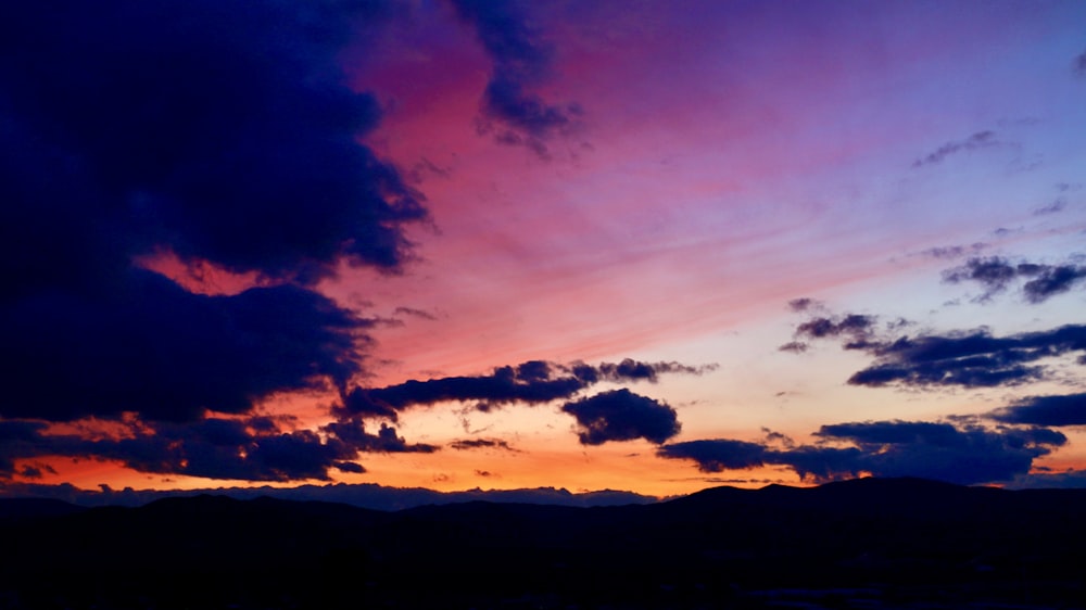 a sunset with clouds and mountains in the background