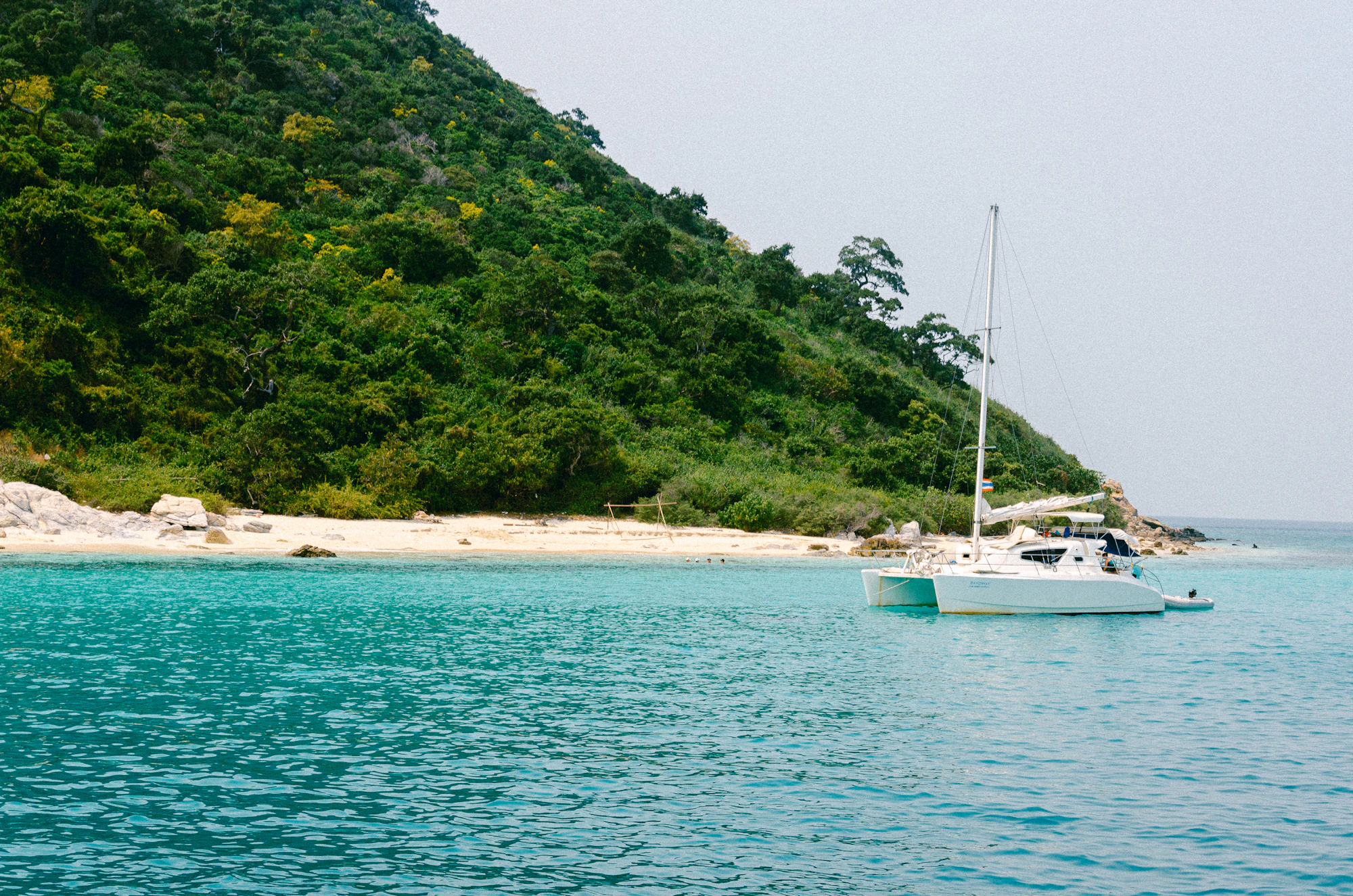 A sailing catamaran under way through turquoise tropical water