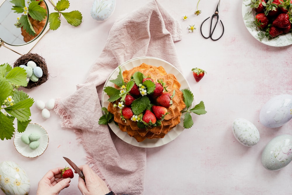 a person cutting strawberries on top of a cake