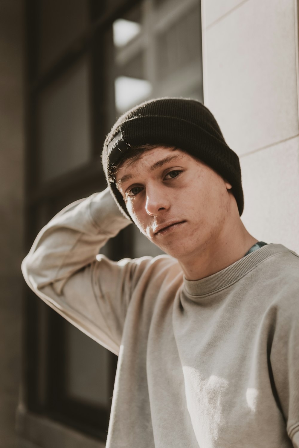 a young man wearing a beanie leaning against a wall