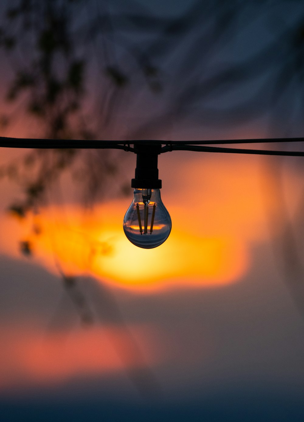 a light bulb hanging from a wire with a sunset in the background