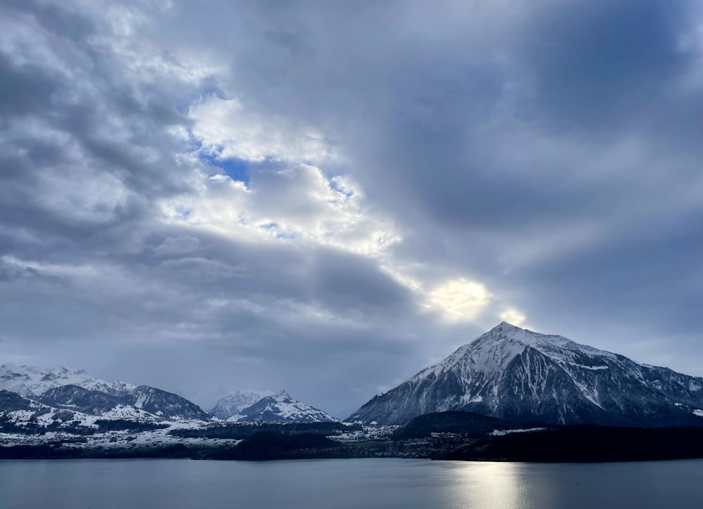 a mountain with a lake below it under a cloudy sky