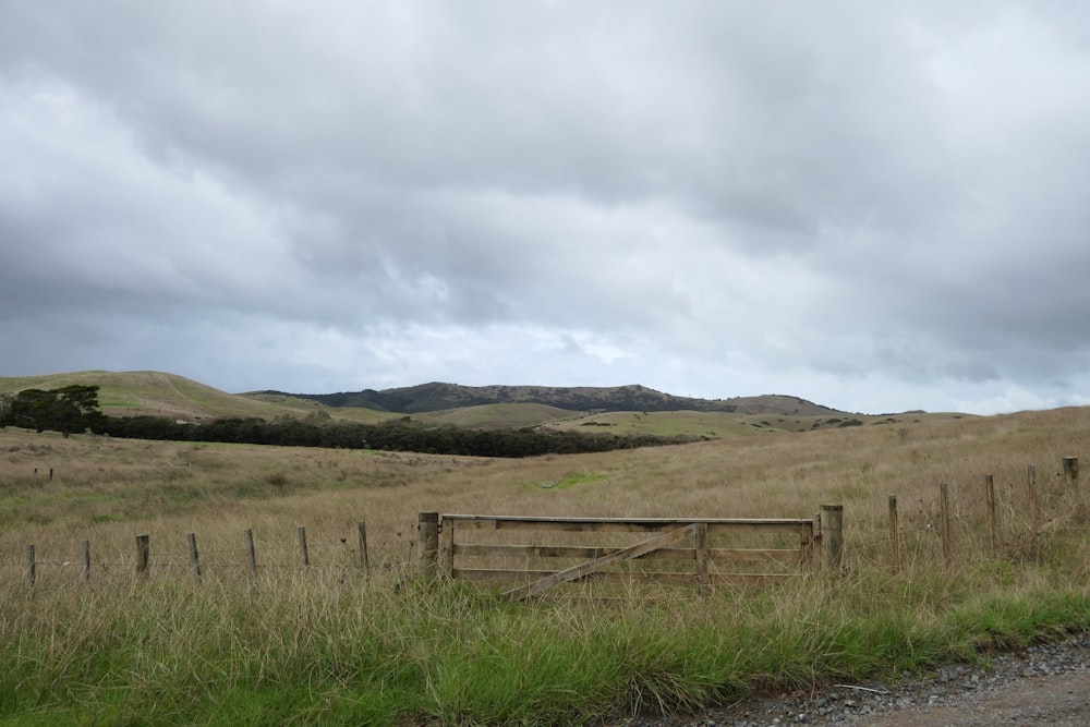 a wooden fence in a grassy field with mountains in the background