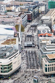 A lively city street view showing modern apartment buildings with people walking and greenery around.