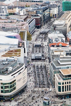 A lively city street view showing modern apartment buildings with people walking and greenery around.