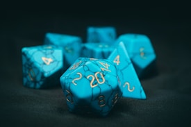 A collection of blue, marble-patterned polyhedral dice with gold numbers, resting on a dark surface.