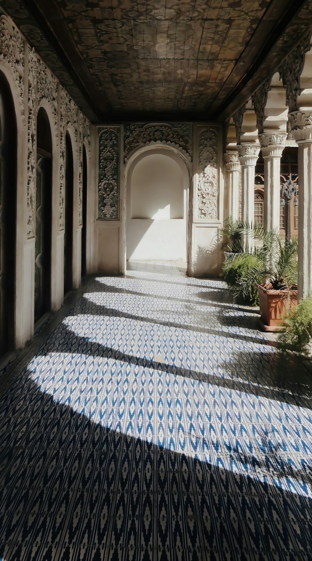 a long hallway with blue and white tiles and potted plants