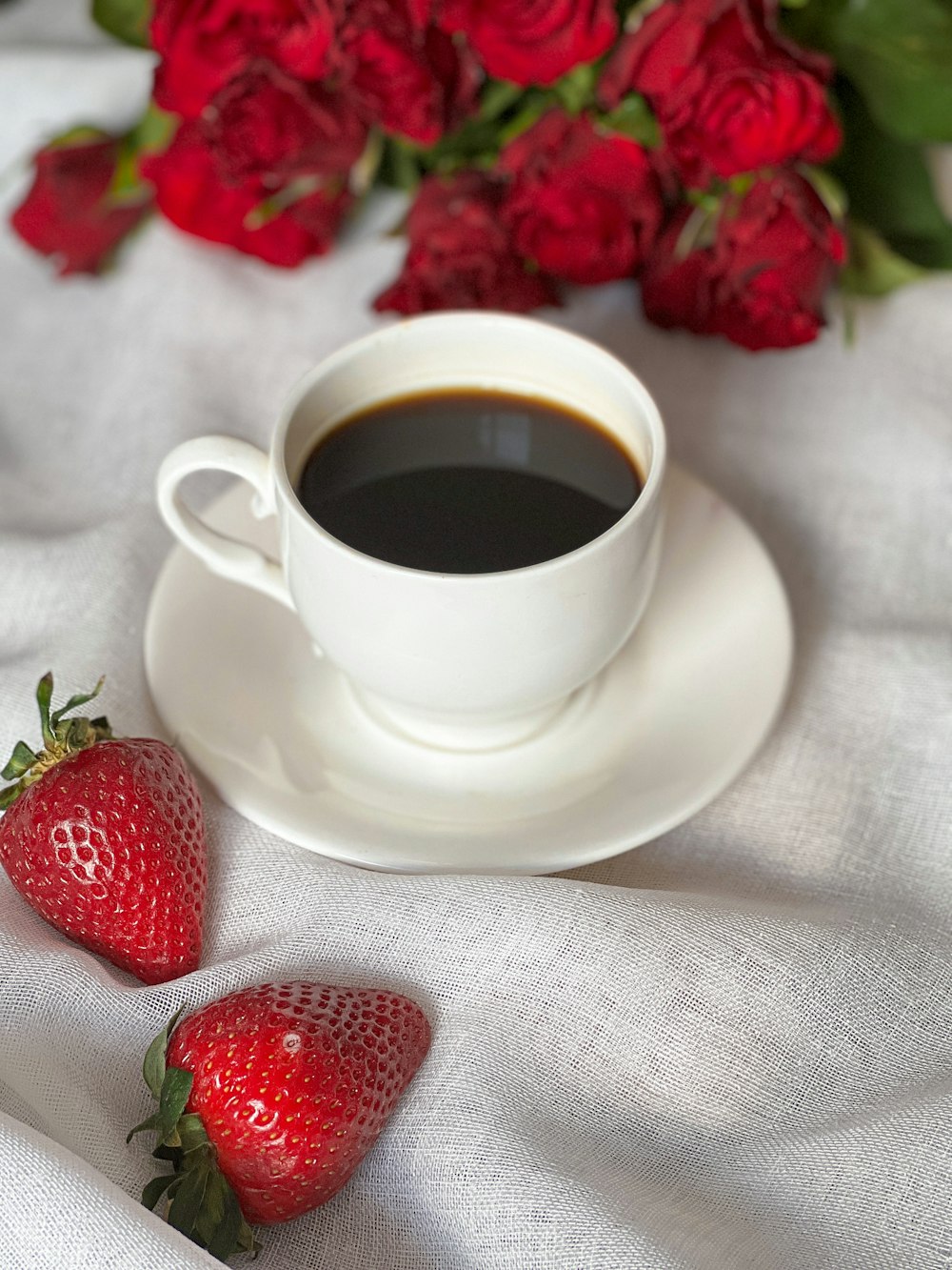 a cup of coffee and two strawberries on a white cloth