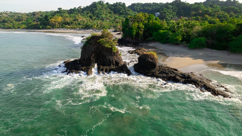 an aerial view of a beach with a rock formation in the middle of the water