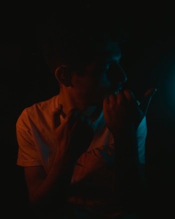 A person is depicted in low lighting, creating dramatic shadows and highlights. The figure is partially obscured, adding an air of mystery. Subtle blue and orange lights play across the scene, suggesting an intimate or contemplative setting.