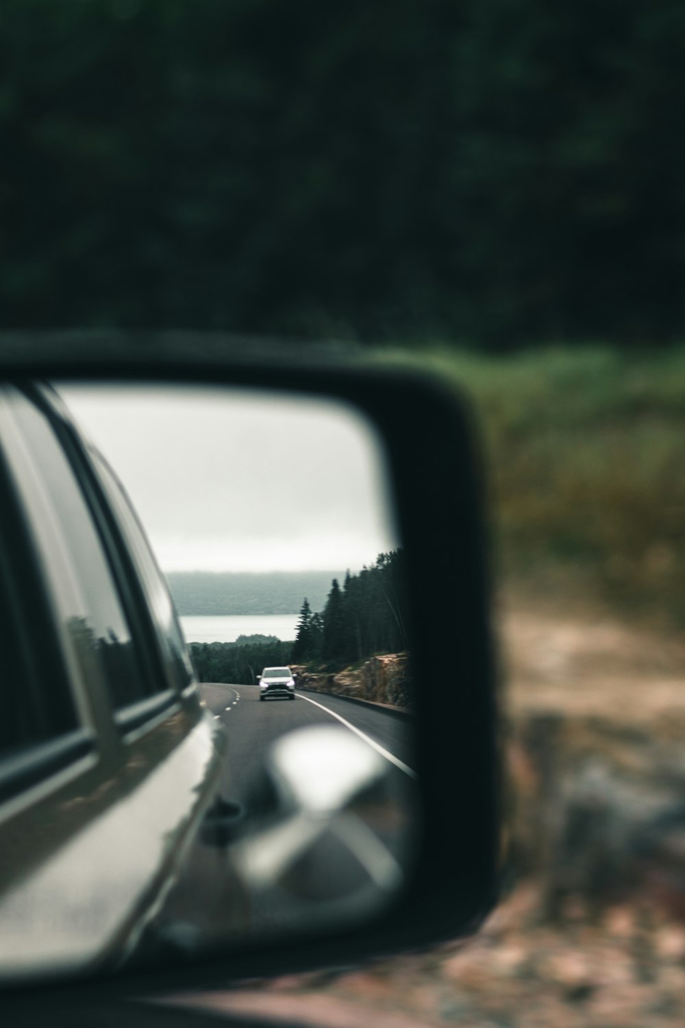 a car's side view mirror reflecting a car's view of a road