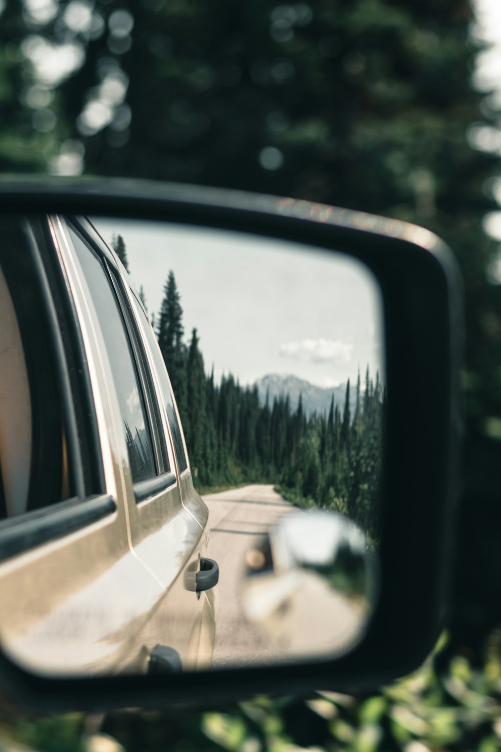 a car's side view mirror reflecting a road in the rear view mirror