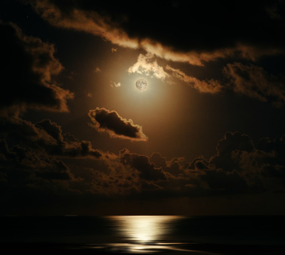 a full moon shines through the clouds over the ocean