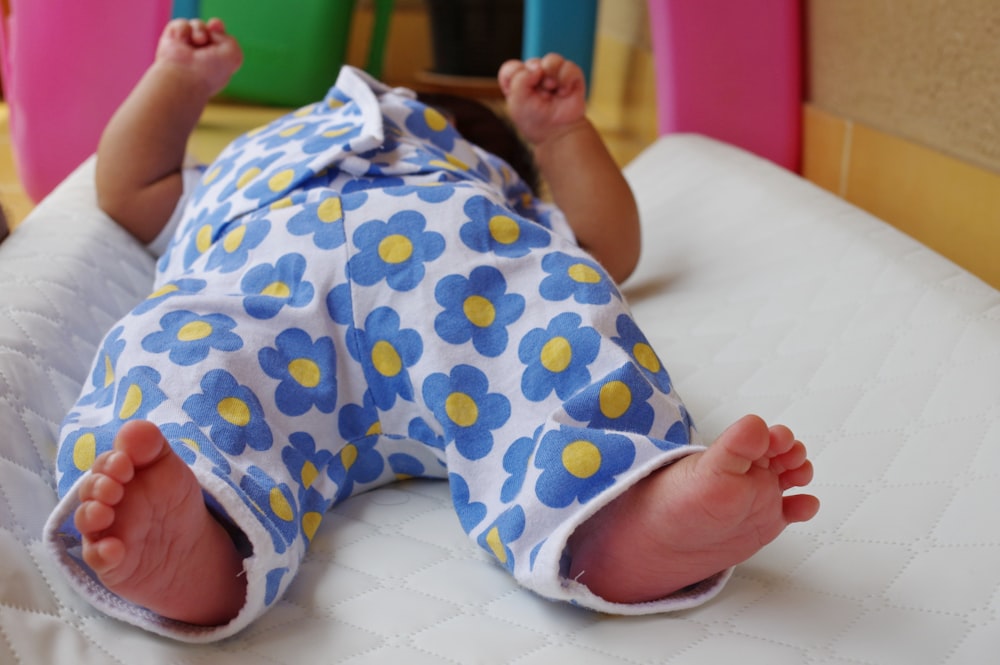 a baby laying on a bed with a blue and yellow flowered outfit