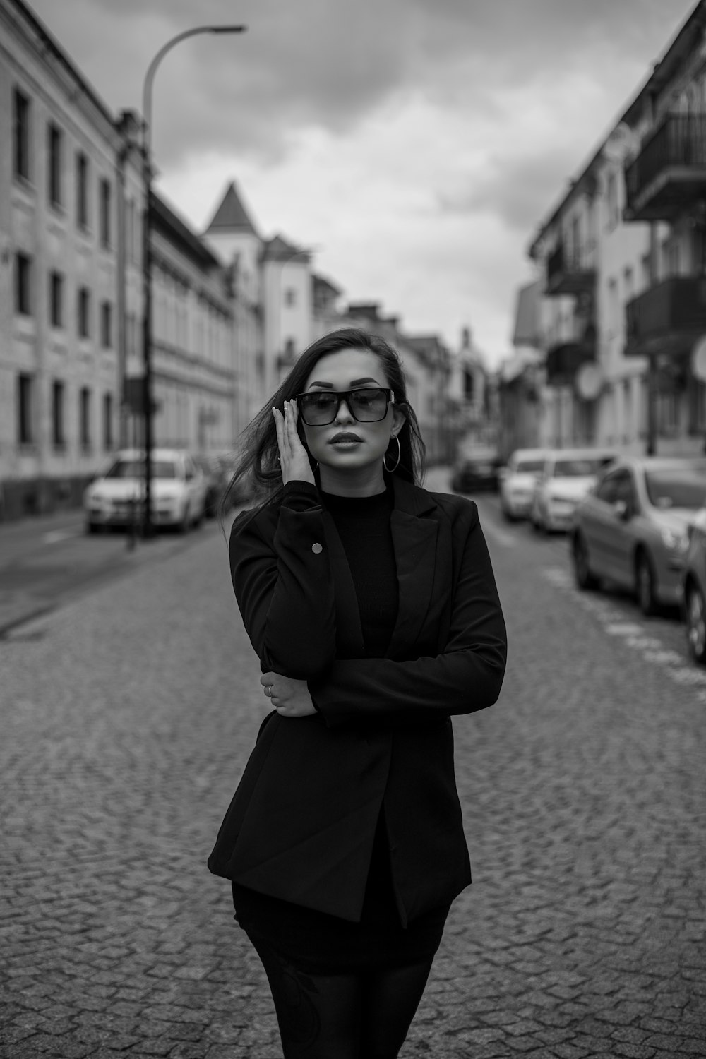 a woman with her arms crossed standing on a cobblestone street