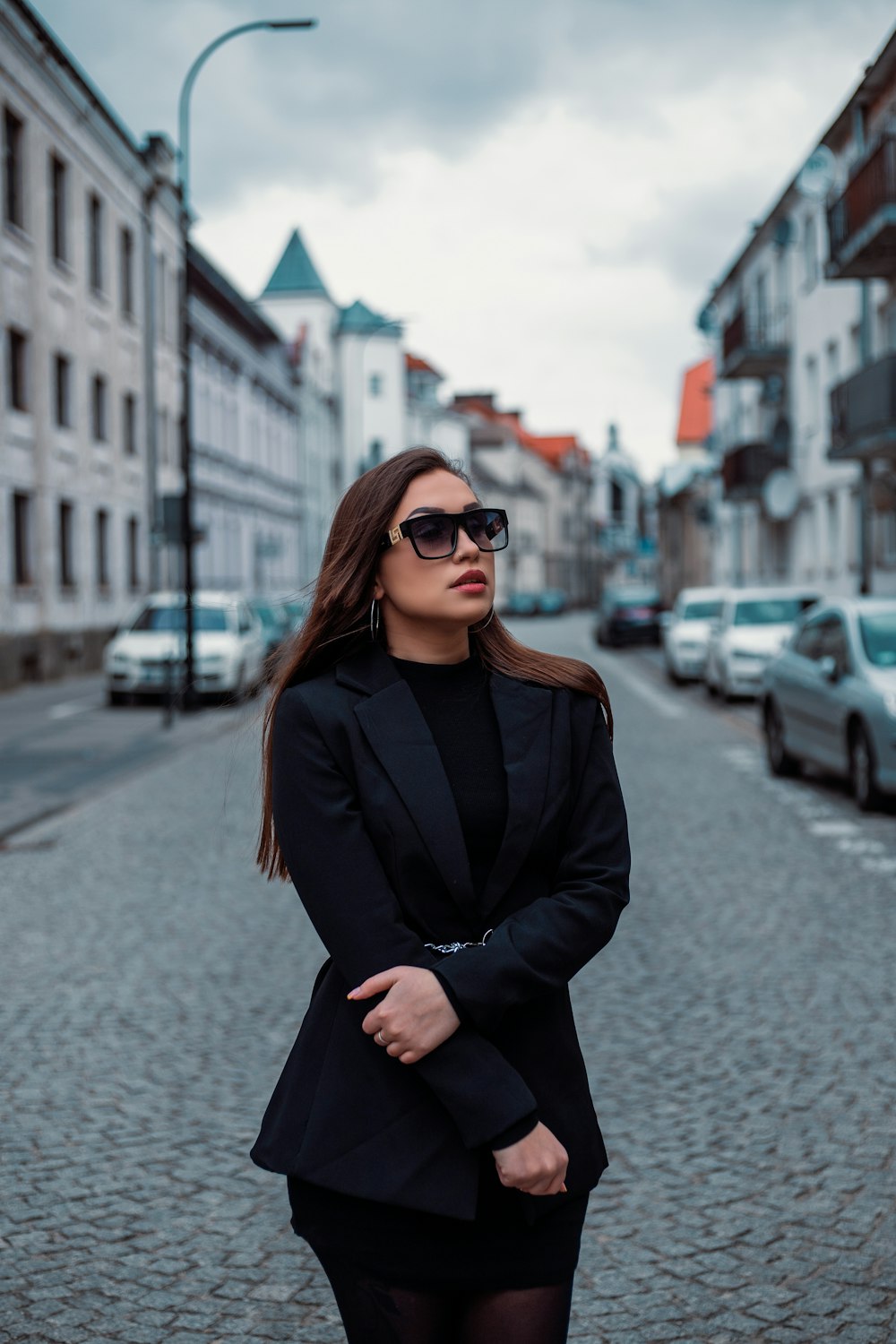 a woman in a suit and sunglasses standing on a cobblestone street