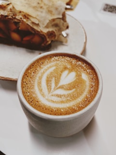 A cozy ceramic mug with a warm latte and a delicate leaf design on the side