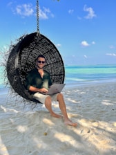 a man sitting in a hanging chair on the beach