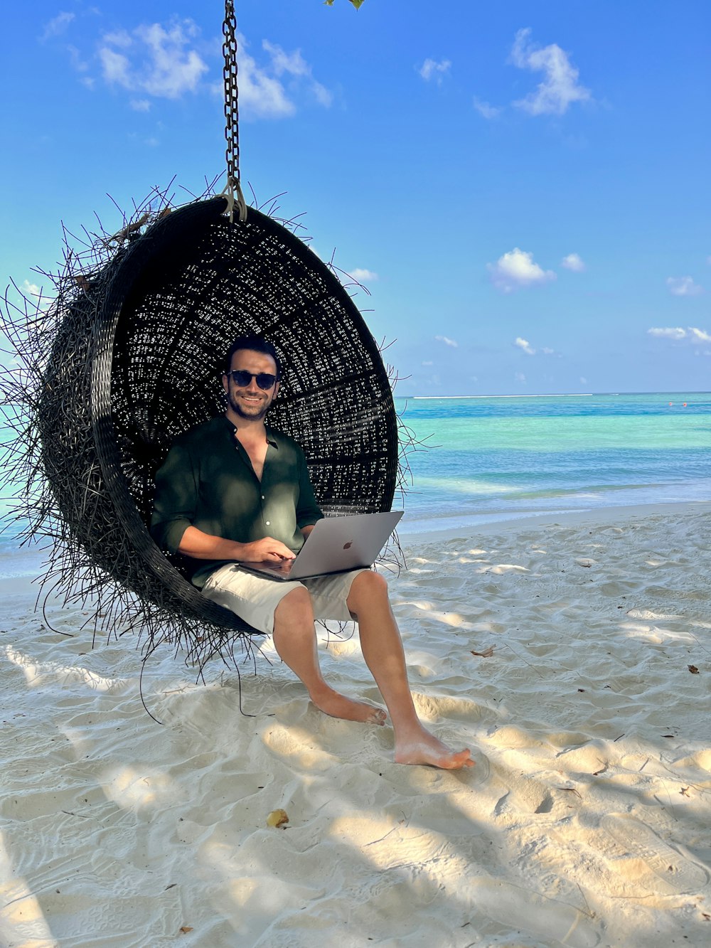 a man sitting in a hanging chair on the beach