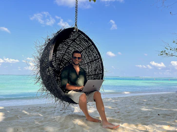 a man sitting in a hanging chair using a laptop computer