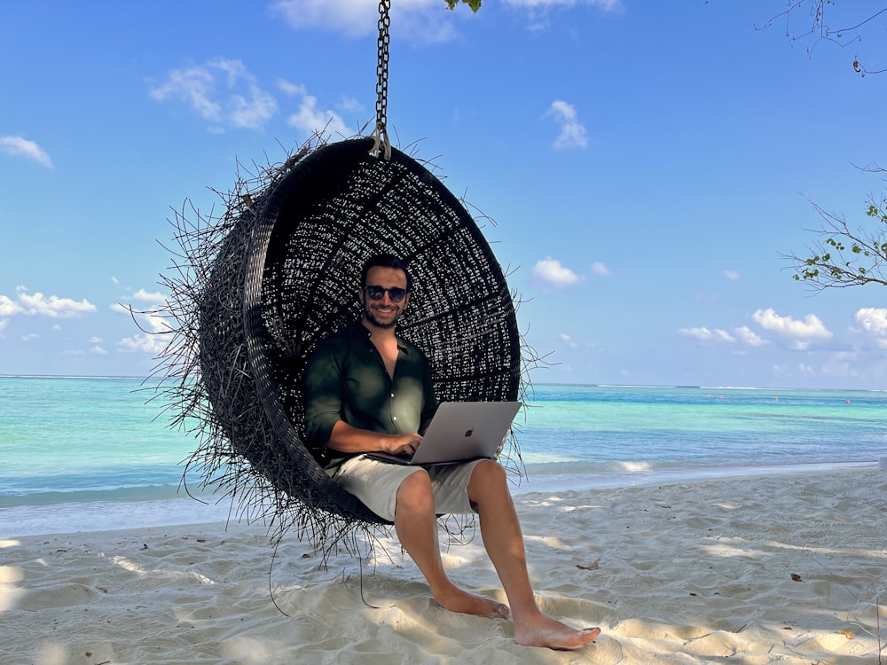 a man sitting in a hanging chair using a laptop computer