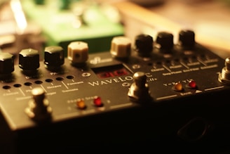 A close-up view of a music pedal or effects processor, featuring various knobs, switches, and an LED display. The surface has labels indicating functions like 'rate,' 'depth,' and 'pattern.' The lighting creates a warm, focused atmosphere.