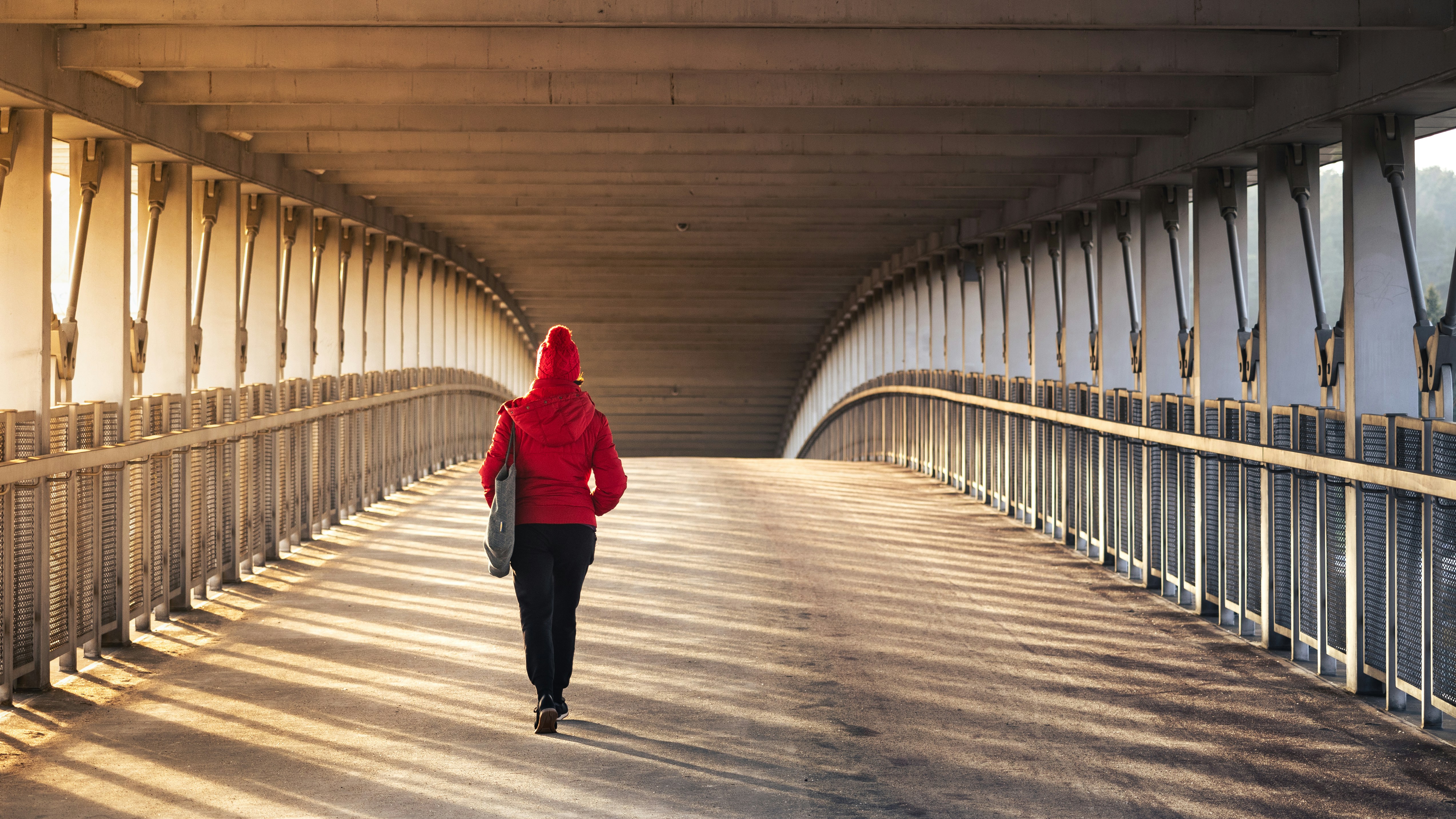 A woman in a red jacket is walking across a bridge