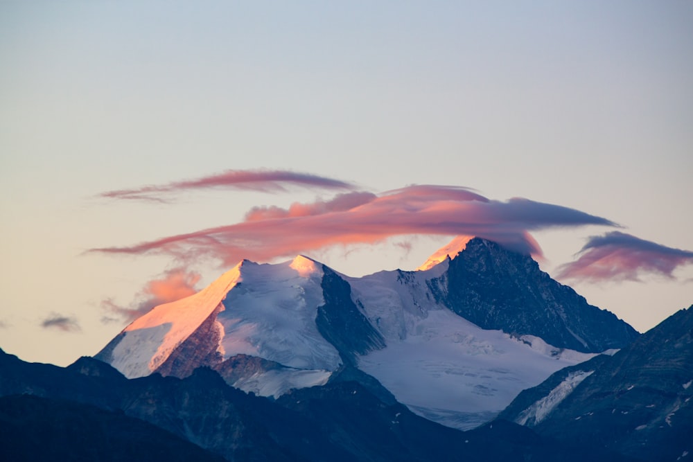 a snow covered mountain with pink clouds in the sky