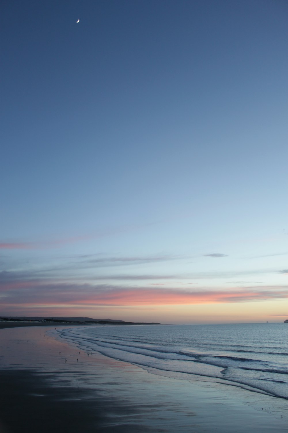 a view of a beach at sunset with the moon in the sky