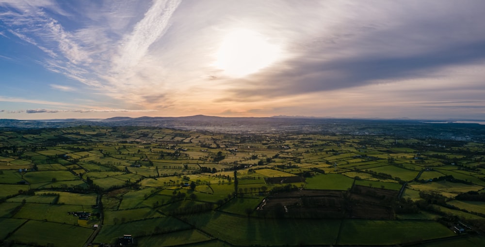 an aerial view of a green field with a sunset in the background