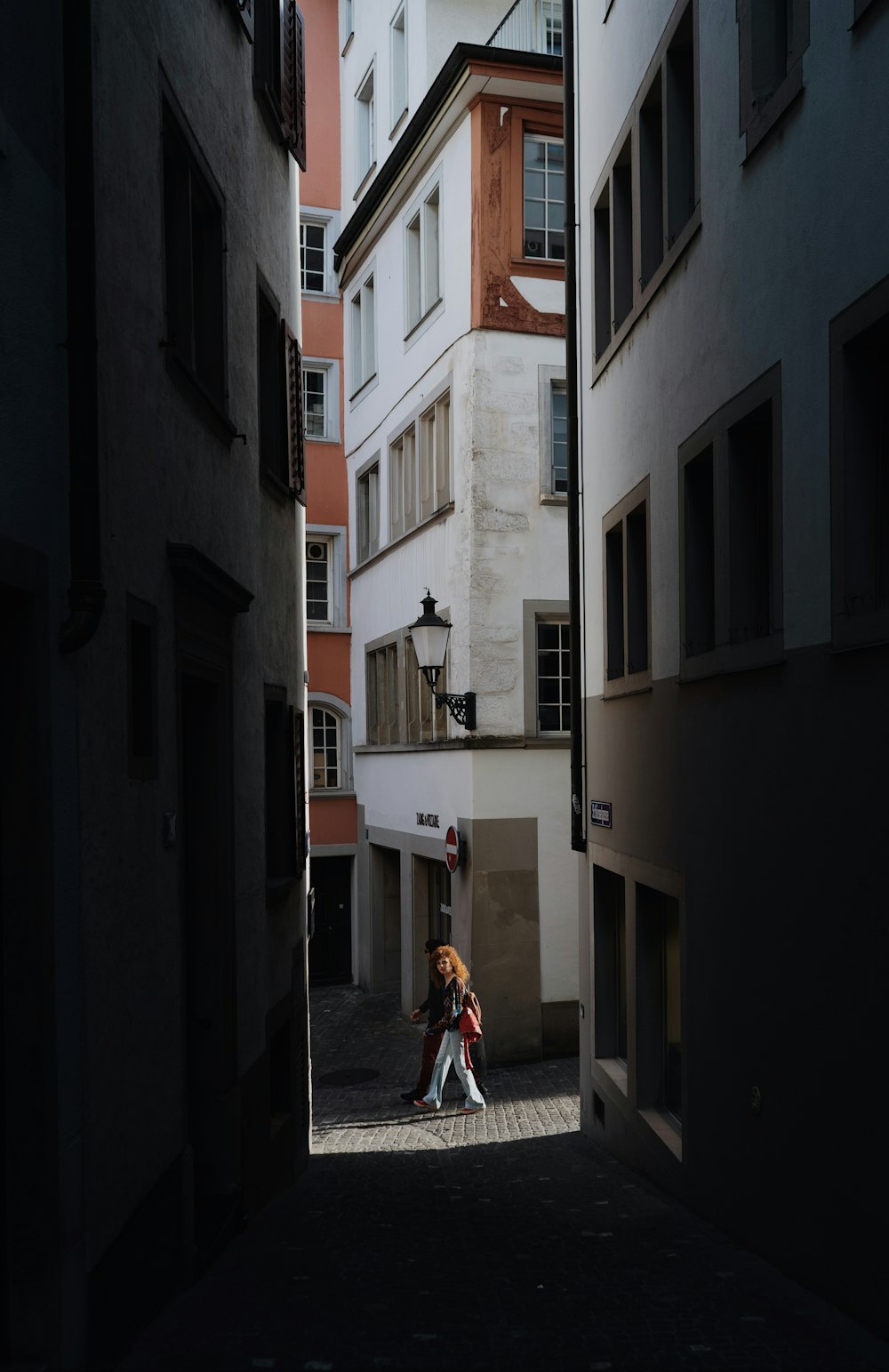 a couple of people walking down a street next to tall buildings