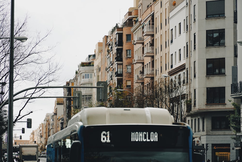 a blue and white bus driving down a street next to tall buildings