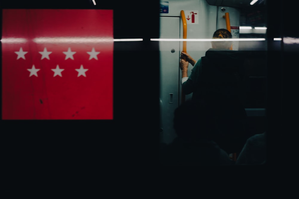 a person sitting on a train next to a red sign