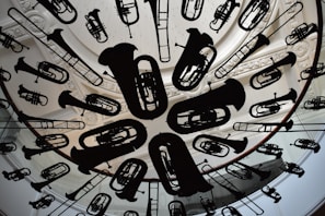A circular ceiling installation features a variety of musical instrument silhouettes, including tubas, trumpets, and trombones. The instruments are suspended uniformly, creating an artistic and dynamic visual effect. The background includes ornate architectural details, such as carved molding and skylight structures.