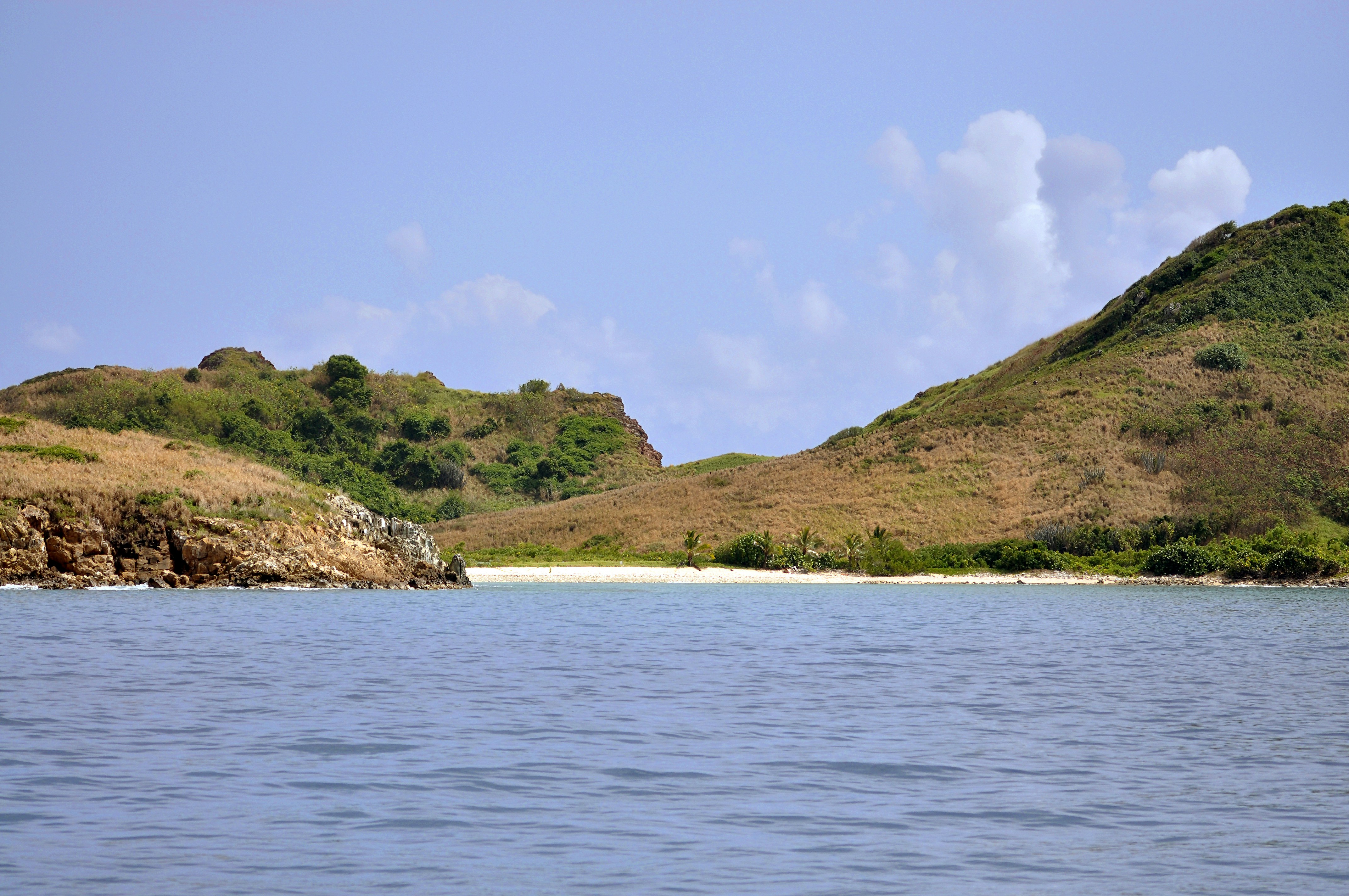 A view from the water looking towards a small Caribbean island with hills and beach.