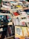 A collection of various books and magazines spread out on a table, with different sizes, colors, and cover designs. The selection includes novels, educational books, and periodicals, some with Spanish titles. The arrangement seems casual, possibly indicating a market or a book fair setting.