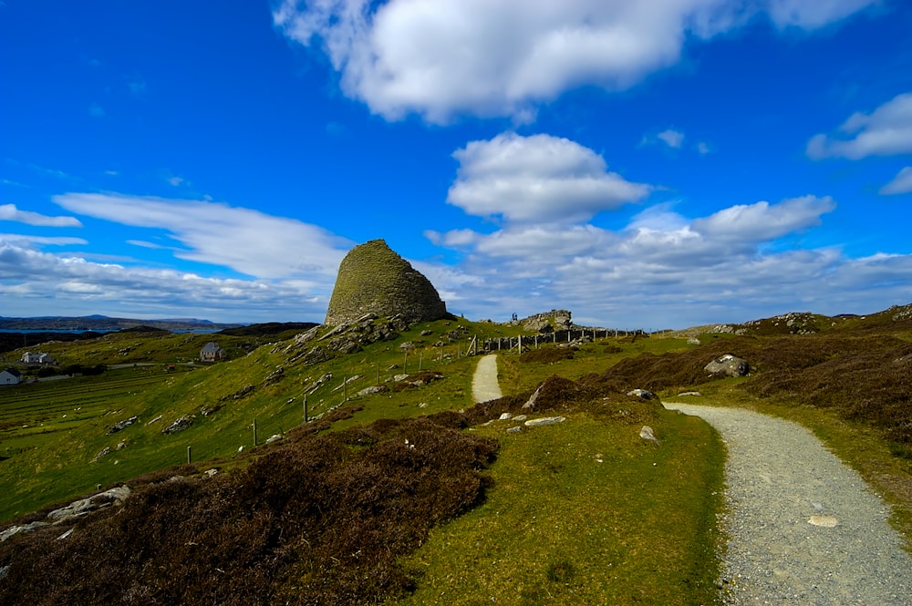 a grassy hill with a path leading to a large rock