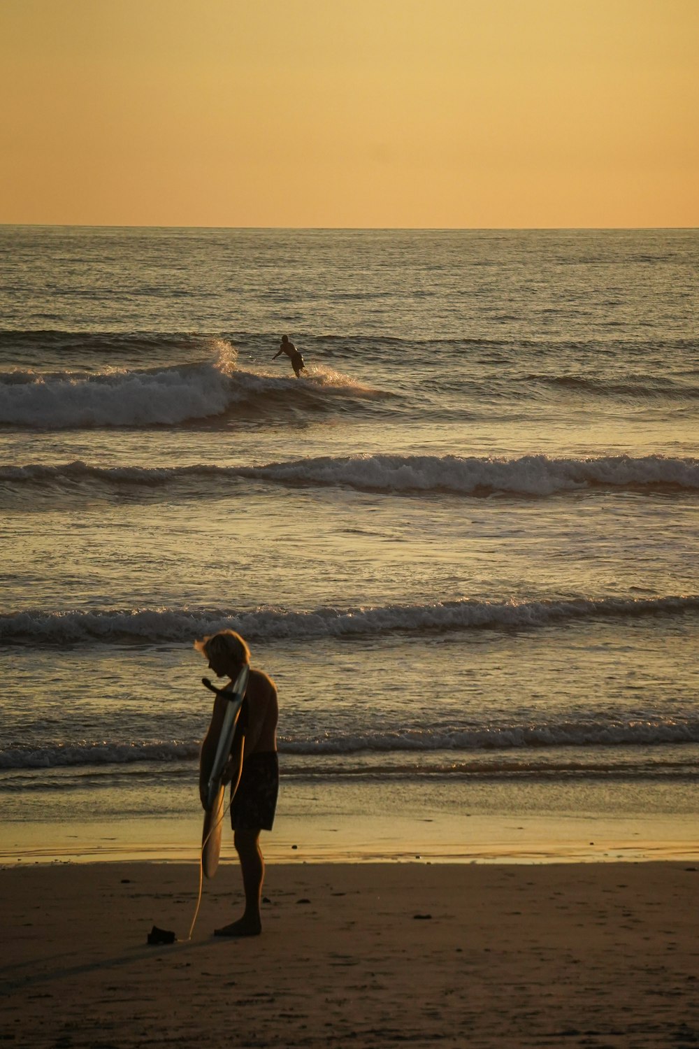 a man standing on top of a beach holding a surfboard