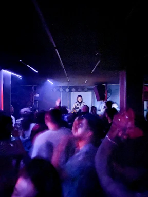 A lively crowd enjoying a night of live music with a band, karaoke singers, and a DJ spinning tracks.