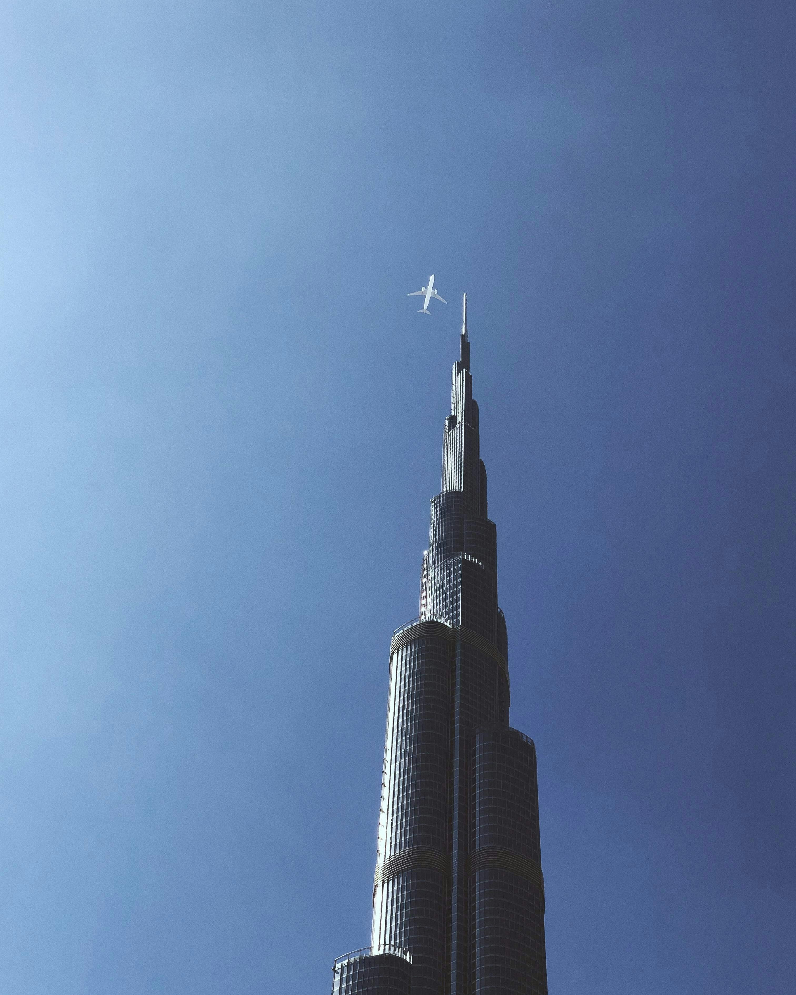 A plane flying in the sky over a tall building photo – Free Dubai Image ...