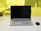 A laptop with a black screen is placed on a white desk. Next to it, on the right side, is a black wireless mouse. The background shows a yellow-tinted glass partition with a blurred view of some objects including a pen holder and another item.