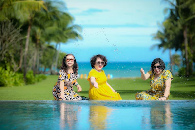 three women sitting on the edge of a swimming pool