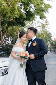 Bride and groom posing near a sleek black electric taxi surrounded by photographers.