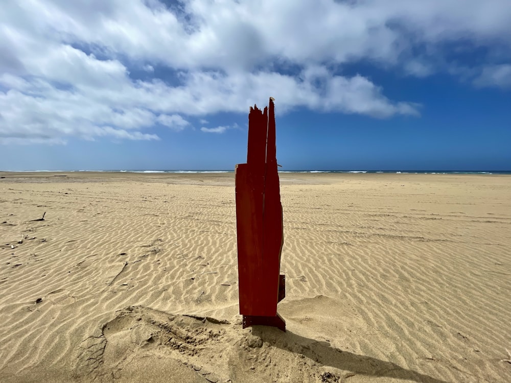 a red piece of art sitting on top of a sandy beach